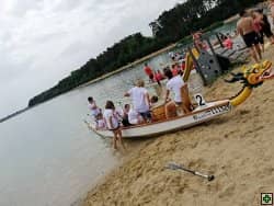 Dračí loď s posádkou na písečné pláži u jezera