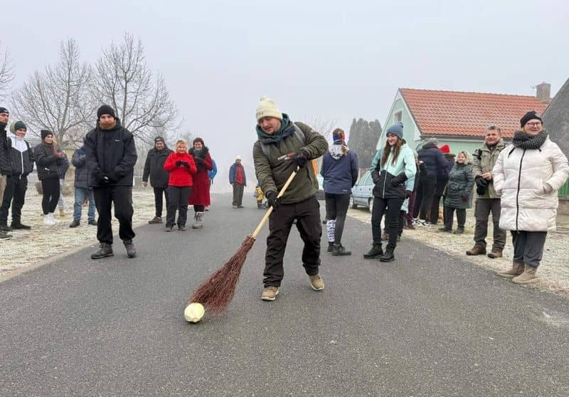 Skupina lidí hraje hru s koštětem a hlávkou zelí na silnici