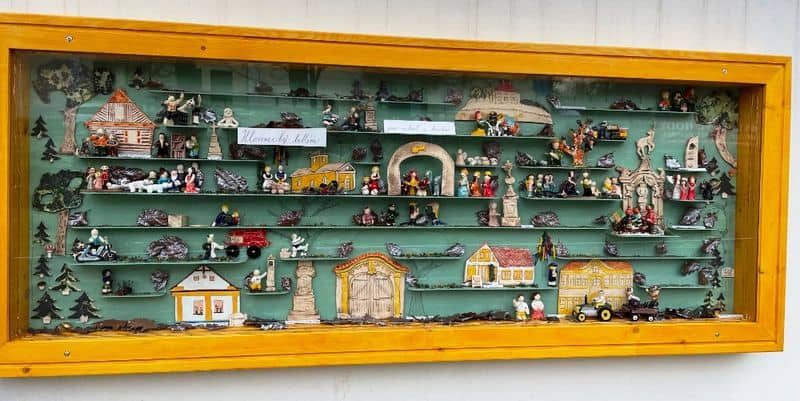 Dřevěná vitrína s miniaturními figurkami a modely domů na zeleném pozadí