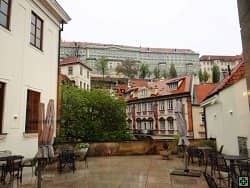 Terasa s kavárenskými stolky a výhledem na historické domy a velkou budovu na kopci