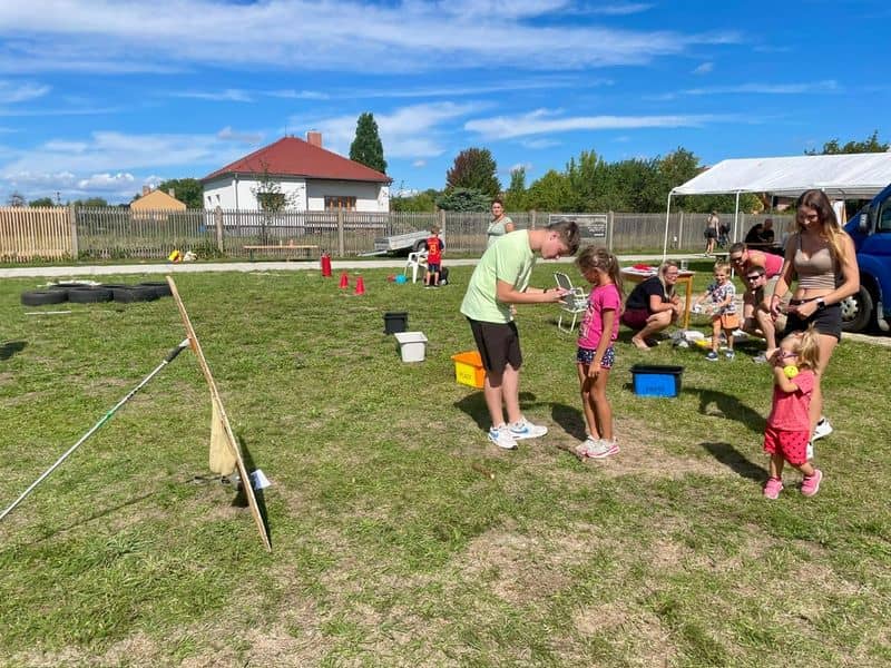 Skupina lidí a dětí na trávníku, v pozadí dům a plot