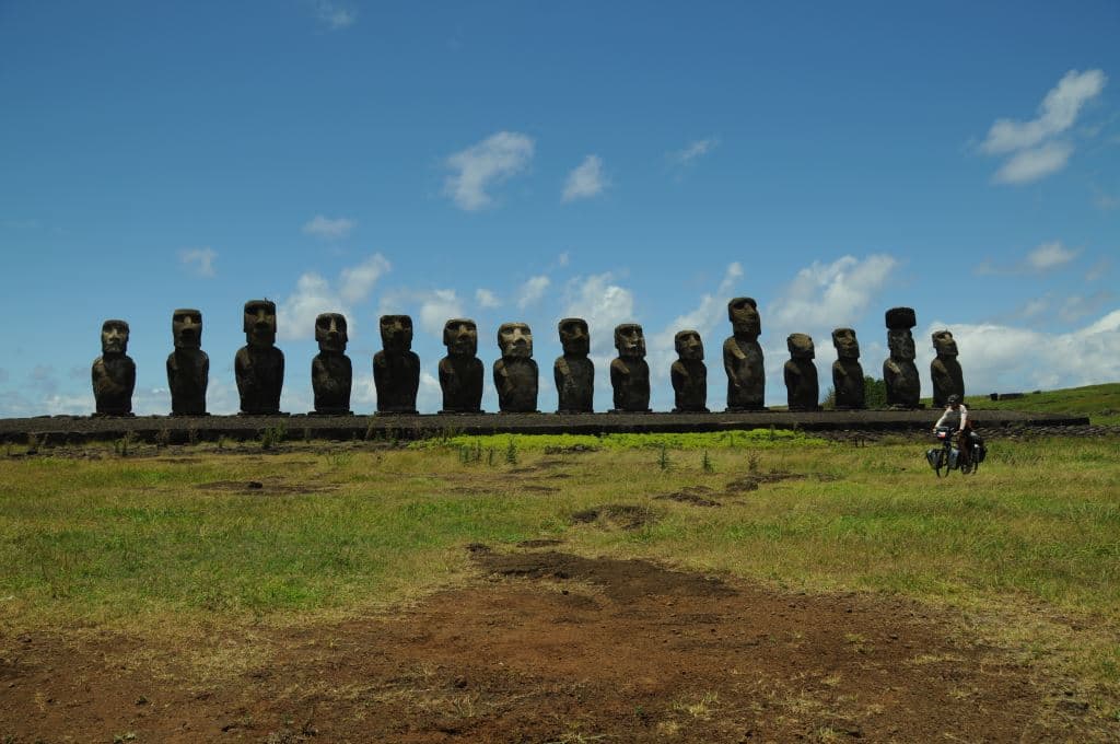 Řada kamenných soch moai na travnaté pláni, vpravo cyklista