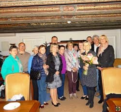 Skupina lidí v místnosti s dřevěným stropem, žena drží kytici