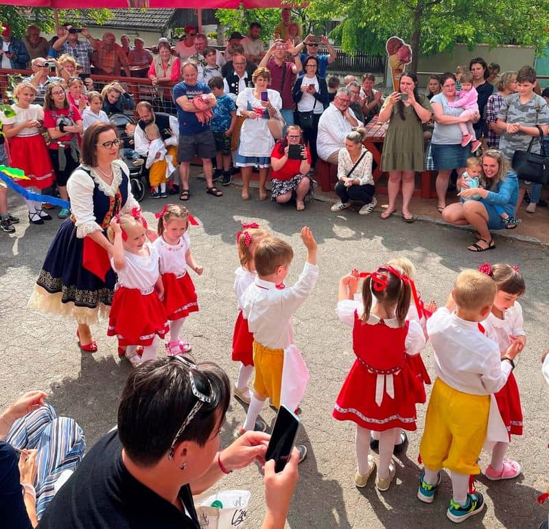 Děti v krojích tančí na ulici, kolem nich stojí a sedí diváci
