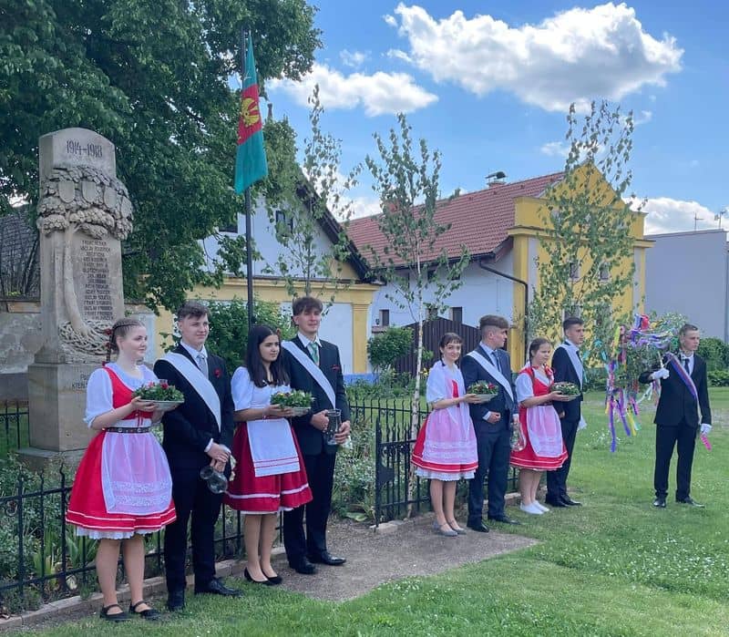 Skupina mladých lidí v krojích a oblecích u pomníku padlých