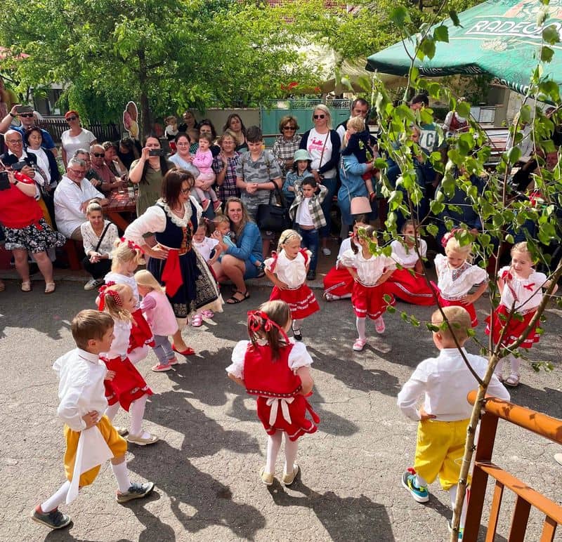 Děti v krojích tančí na venkovní akci, přihlíží skupina lidí