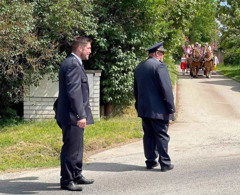 Dva muži v uniformách sledují průvod s koňským povozem