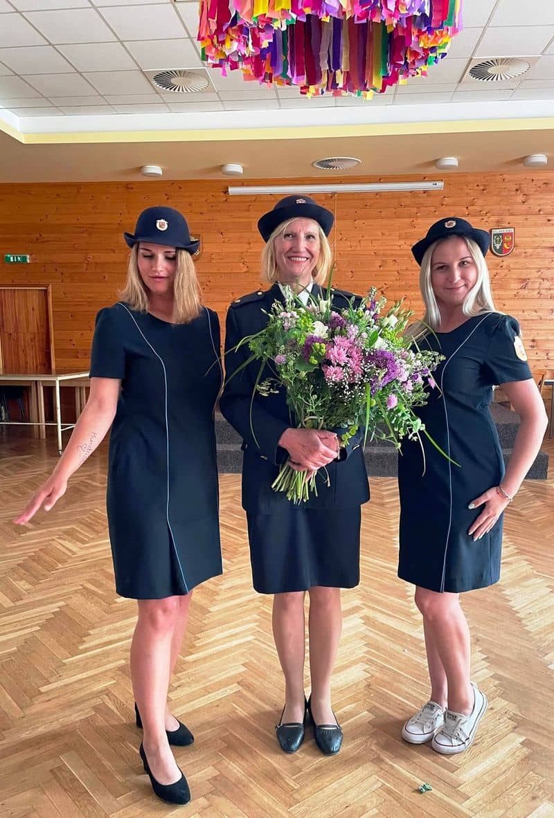 Tři ženy v uniformách s klobouky, jedna drží kytici