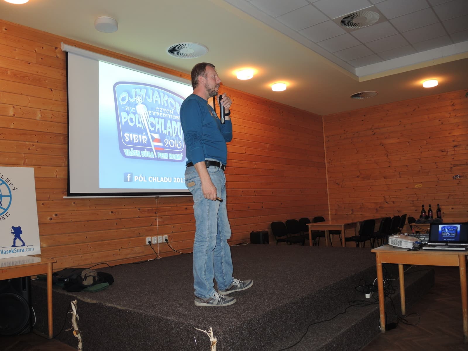 Muž s mikrofonem před plátnem s nápisem Ojmjakon, Pól chladu, Sibiř 2013