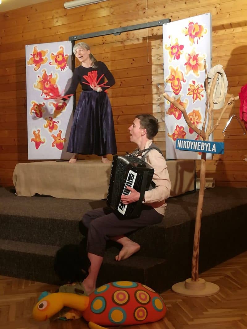 Dva herci na jevišti, žena tančí s vějíři, muž hraje na akordeon