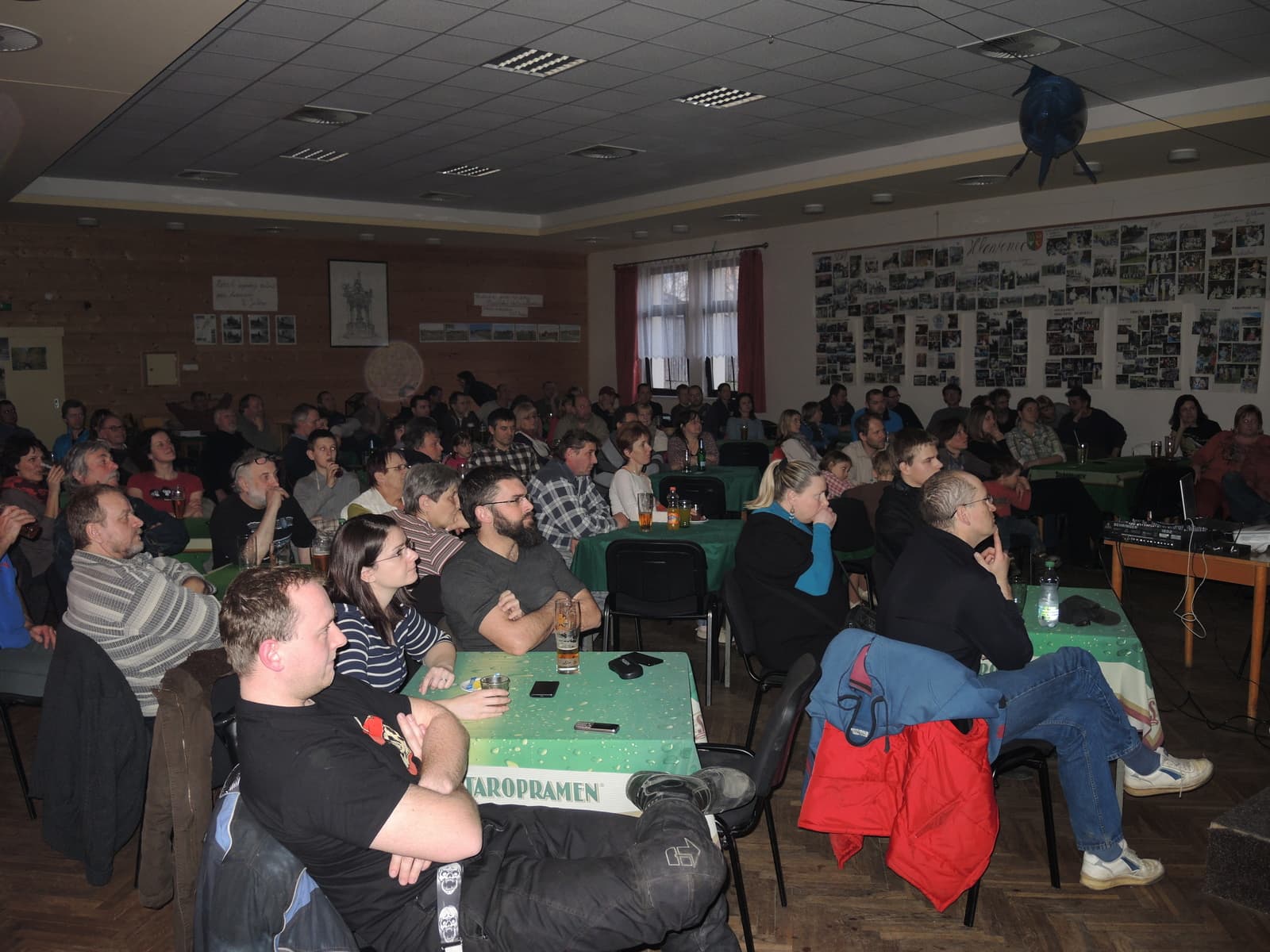 Skupina lidí sedí u stolů v sále a sleduje prezentaci