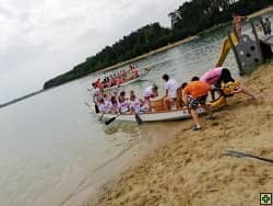 Dračí loď s posádkou na písčité pláži u jezera