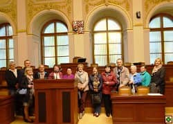 Skupina lidí v historickém sále s dřevěným nábytkem a velkými okny