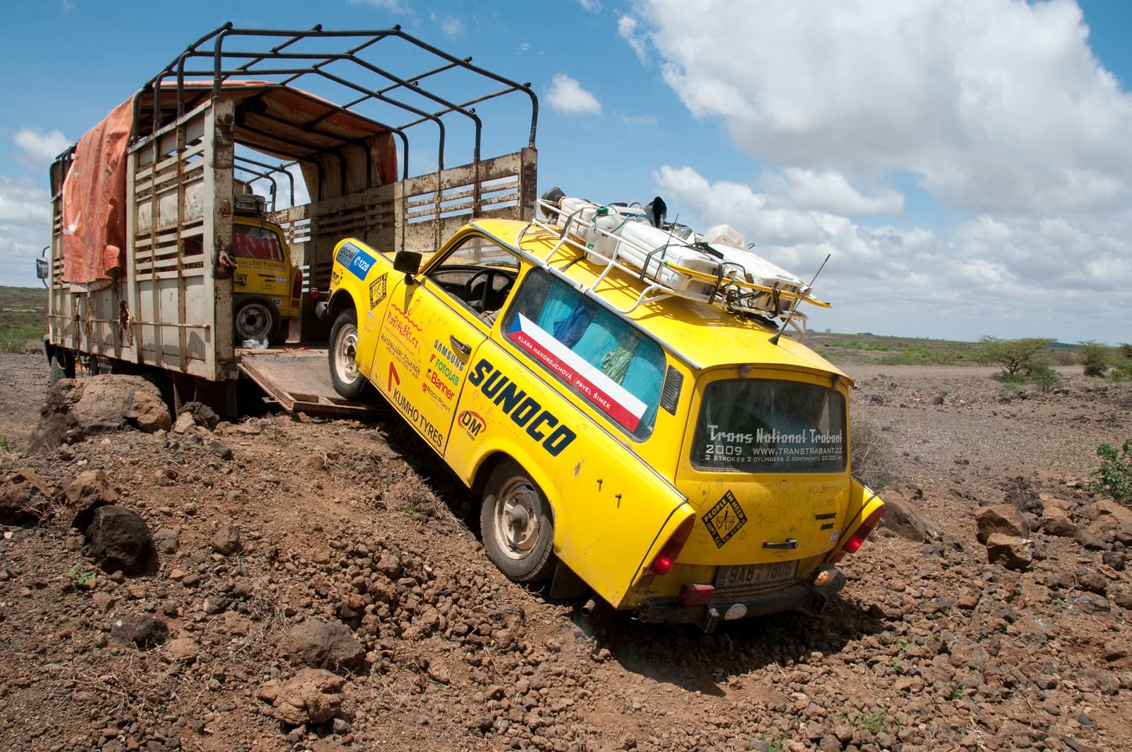Žlutý Trabant s nákladem na střeše najíždí na rampu nákladního auta