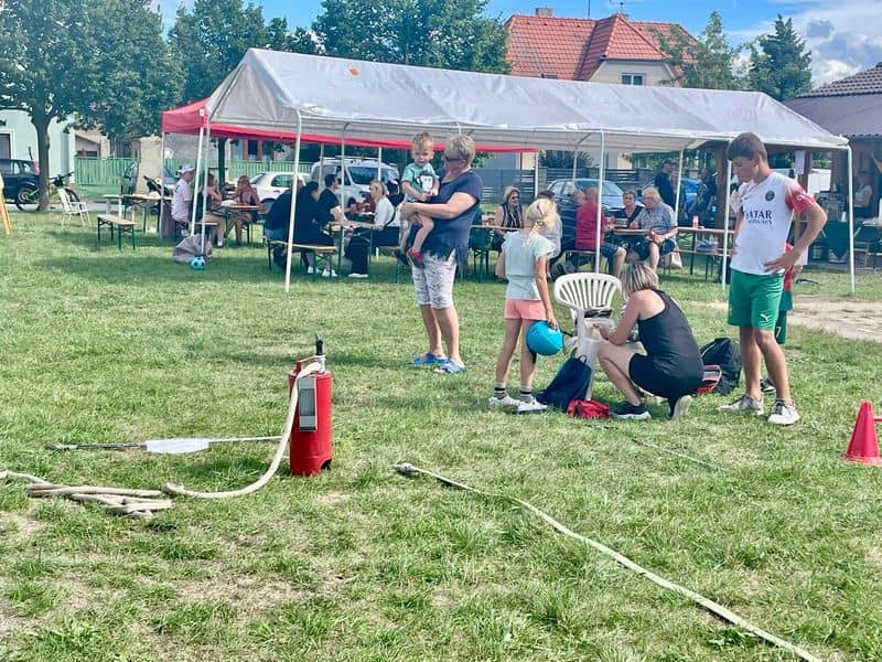Skupina lidí na trávě pod stanem, v popředí hasičské vybavení