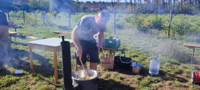 Muž míchá jídlo v kotlíku, kolem je kouř