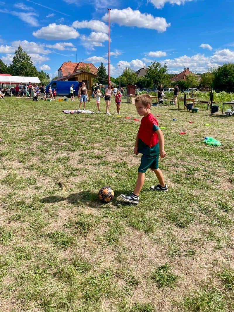 Chlapec hraje fotbal na trávě, v pozadí skupina lidí