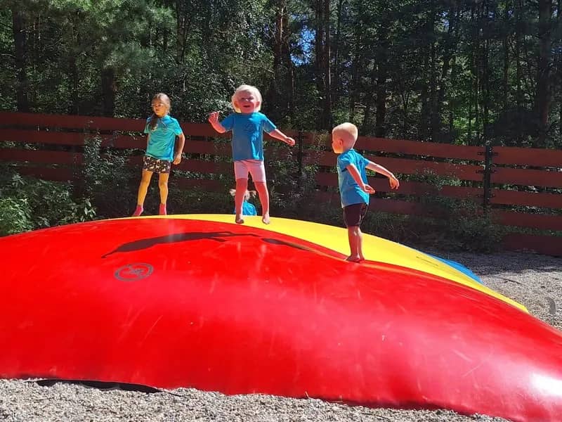 Děti skáčou na velké červené nafukovací trampolíně.