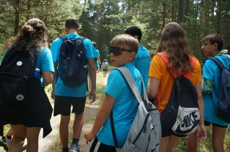 Děti s batohy a modrými táborovými tričky na výletě.