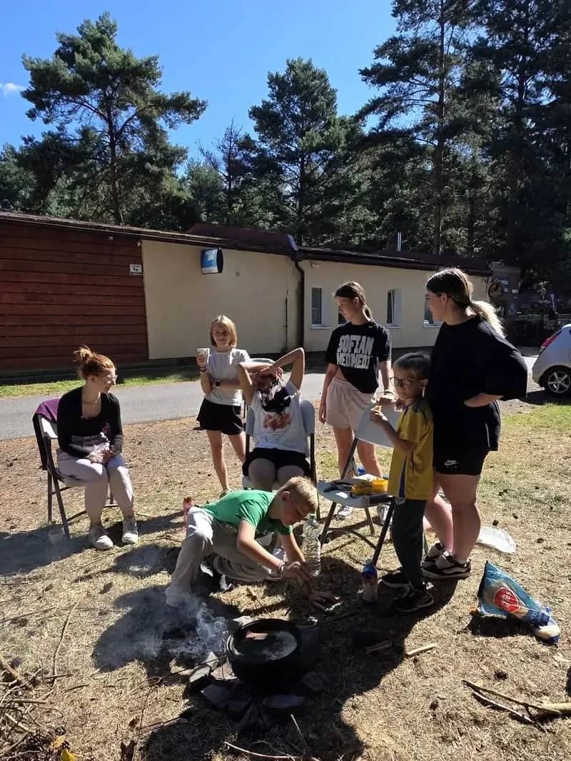 Děti a dospělí kolem ohniště s kotlíkem.