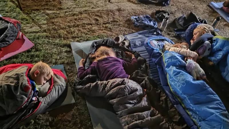 Děti odpočívají ve spacích pytlích pod širým nebem.
