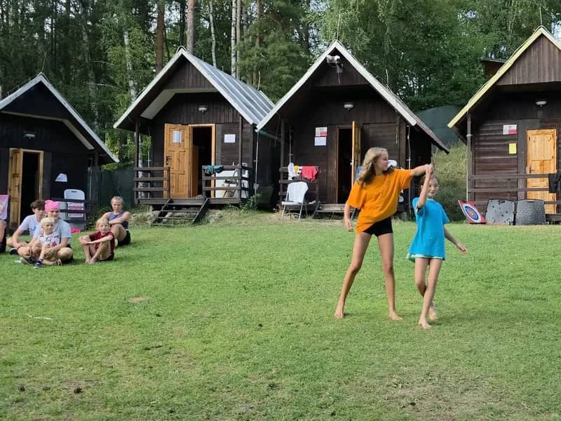 Dvě účastnice při pohybové hře na trávníku před chatkami.