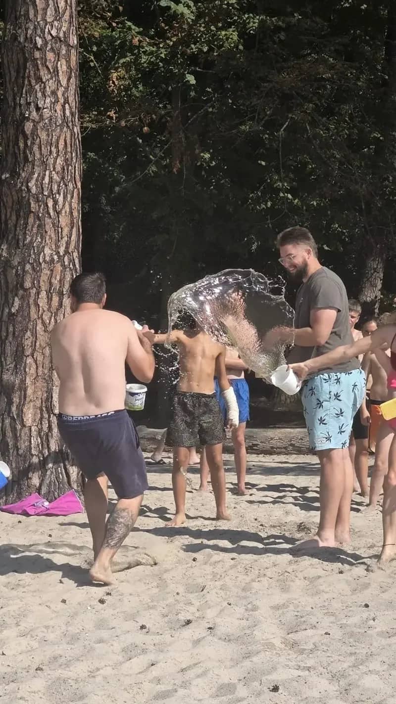 Děti v plavkách se shlukují u stromu během venkovní hry.