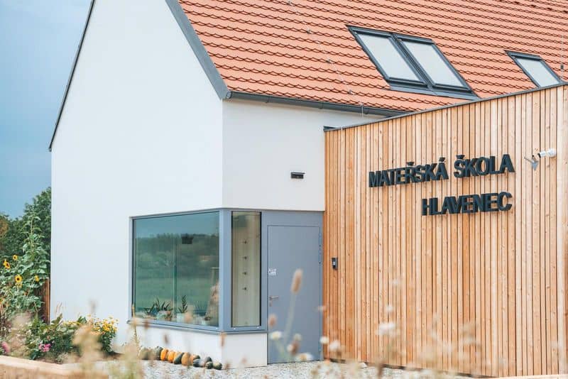 Mateřská škola Hlavenec, moderní budova s dřevěným obložením a červenou střechou