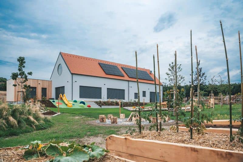 Nová budova mateřské školy se solárními panely a zahradou s hřištěm