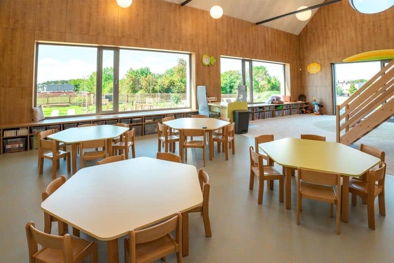 Moderní třída s dřevěnými stoly a židlemi, velkými okny a výhledem do zahrady