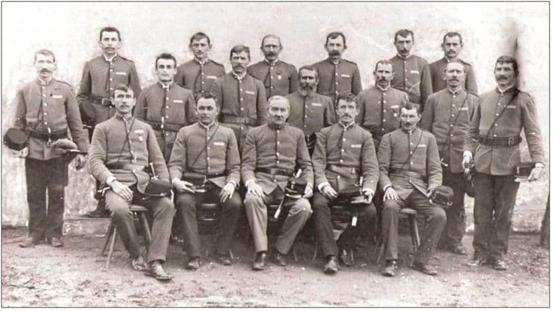 Historická skupinová fotografie členů hasičského sboru ve stejnokrojích, dvě řady stojících a řada sedících mužů