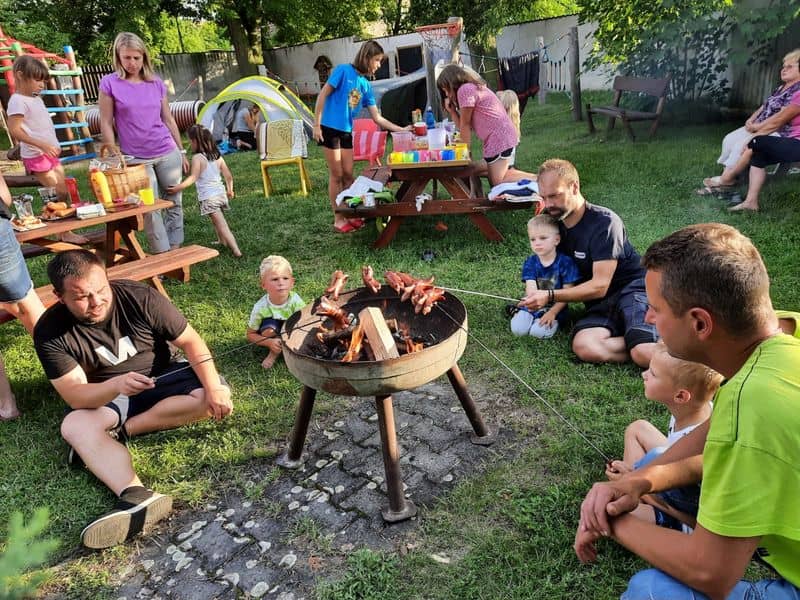 Skupina dospělých a dětí opéká buřty na zahradě