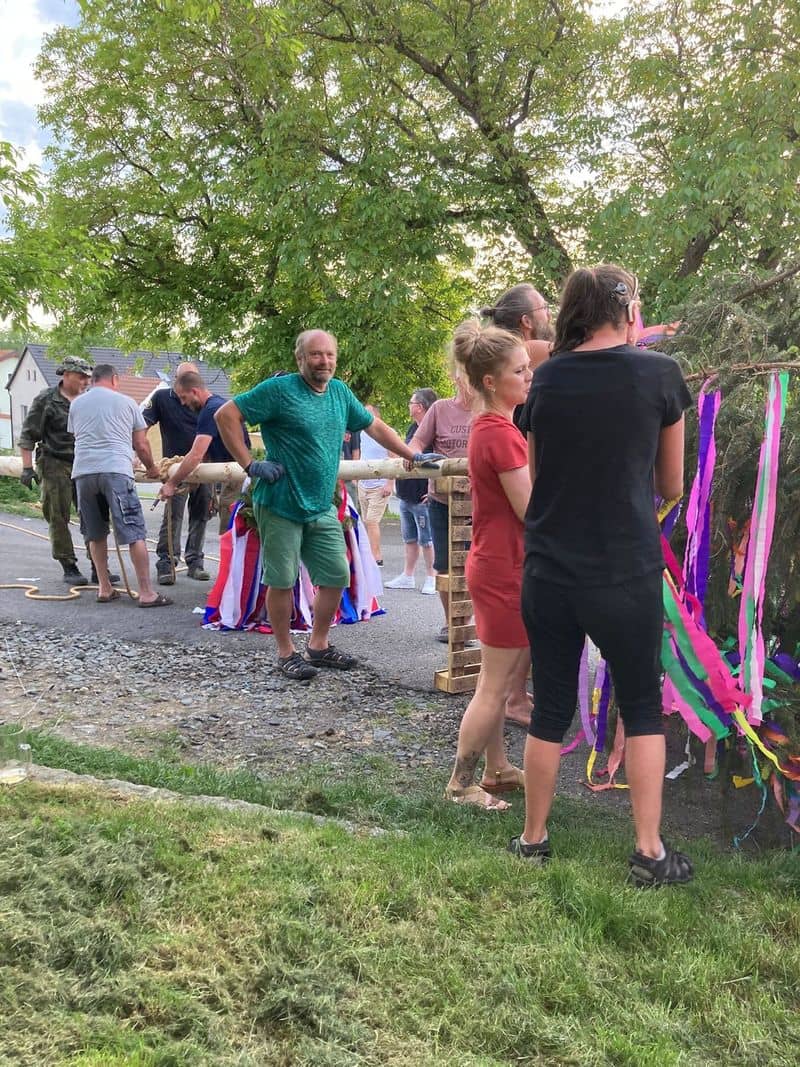 Skupina lidí staví májku ozdobenou barevnými stuhami