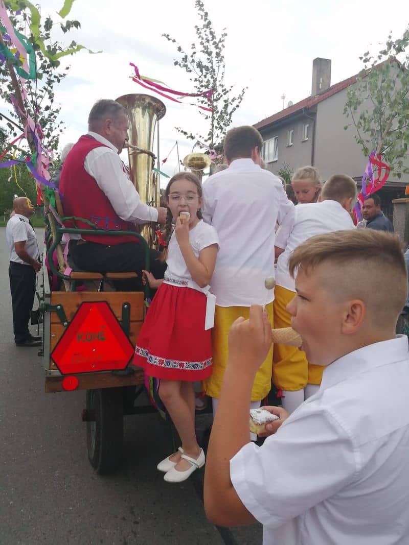 Děti v krojích jedí zmrzlinu a pečivo na voze s muzikantem