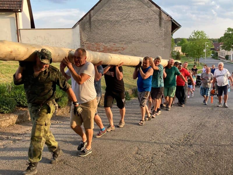 Skupina mužů nese na ramenou dlouhý kmen stromu po silnici