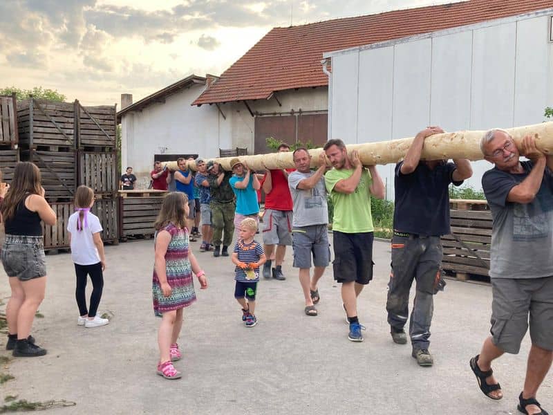 Skupina mužů nese kmen stromu, kolem stojí děti