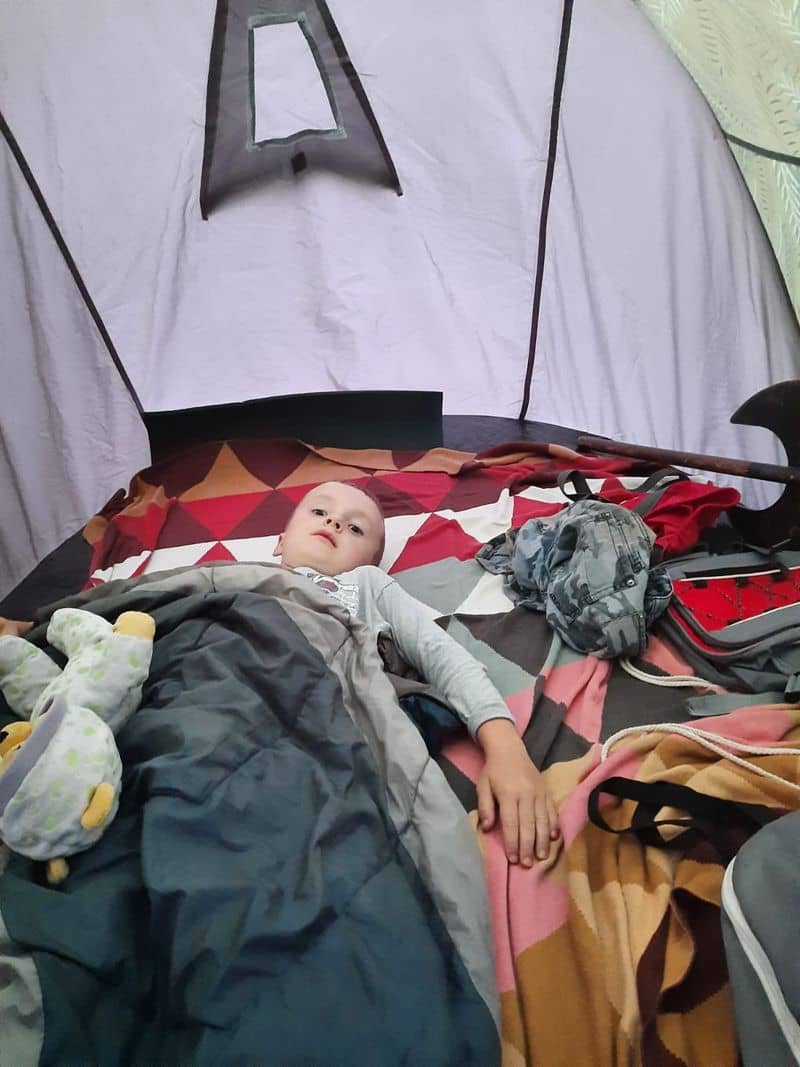 Chlapec leží ve spacáku uvnitř stanu