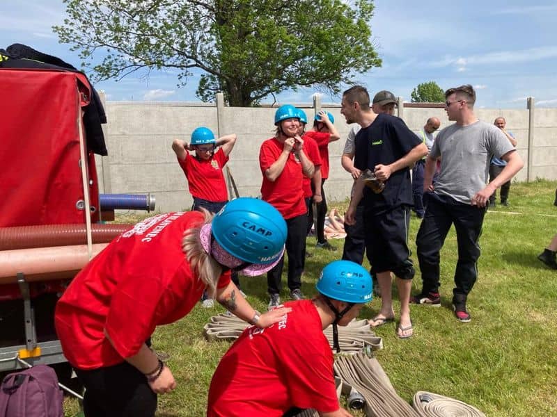 Skupina lidí v červených tričkách a modrých helmách připravuje hasičské hadice
