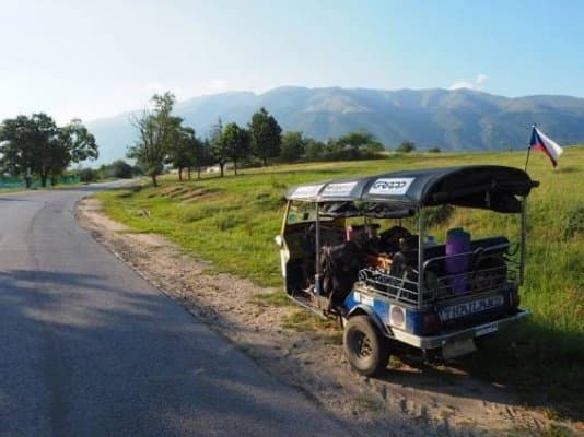 Tuk-tuk s vlajkou u silnice v krajině s horami