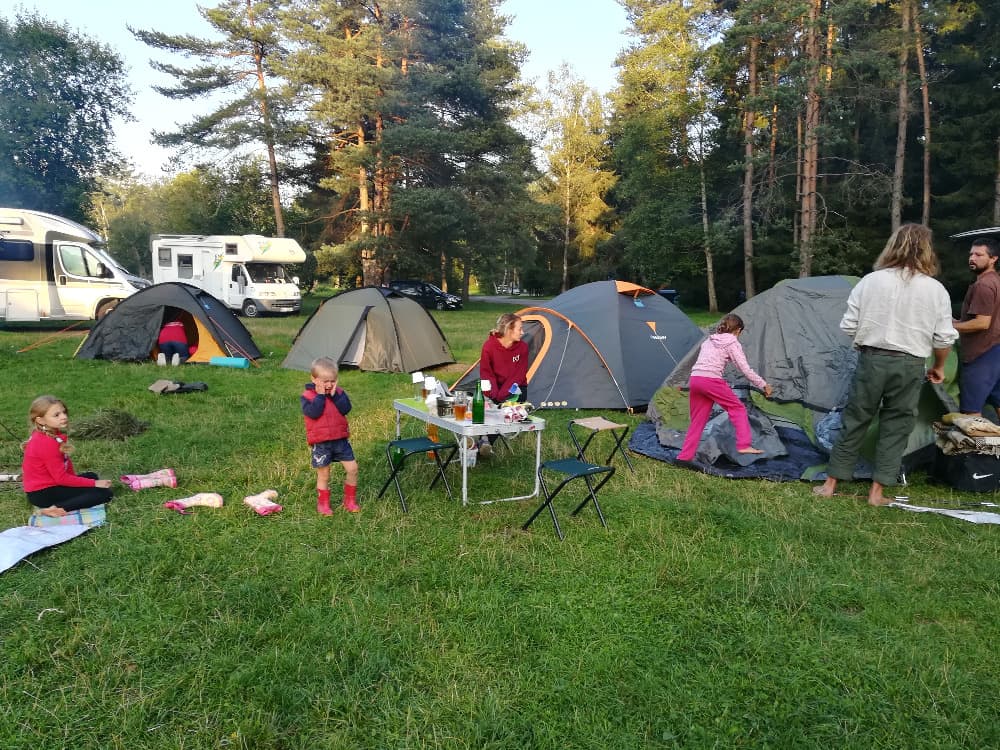 Skupina lidí s dětmi kempuje v lese, staví stany