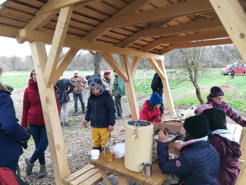 Skupina lidí a dětí pod dřevěným přístřeškem