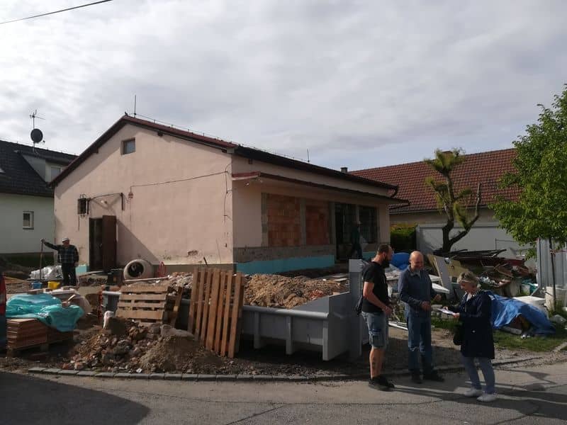 Stavba domu s kontejnerem a třemi lidmi na ulici