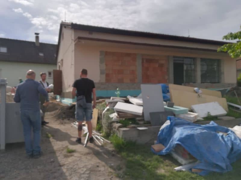 Tři muži u rozestavěného domu s hromadou stavebního materiálu
