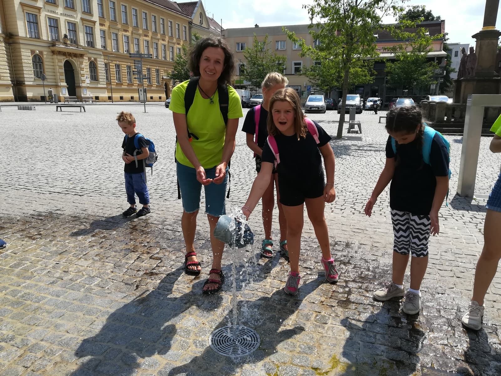 Žena a děti si hrají s vodou na náměstí