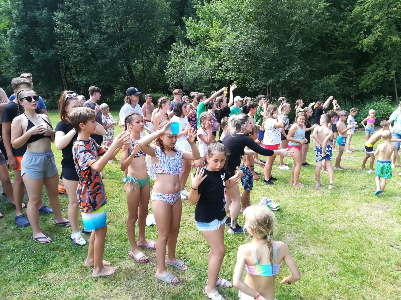 Skupina dětí a dospělých cvičí venku na trávě