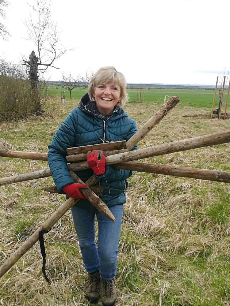 Žena v bundě a rukavicích nese dřevěné kůly