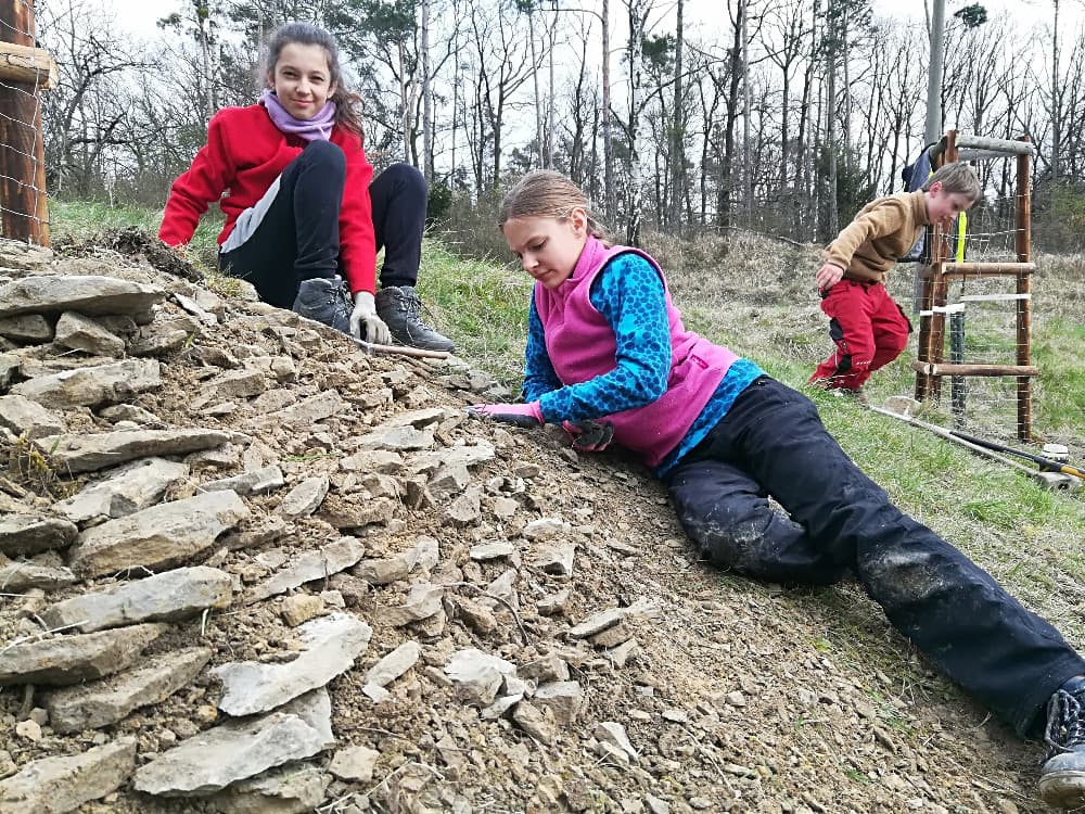 Tři děti pracují na kamenné zídce v přírodě