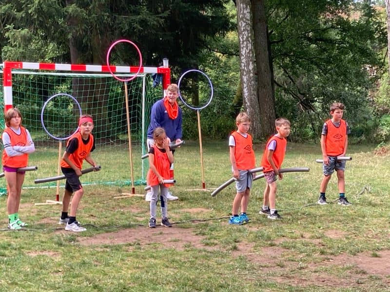 Děti s instruktorem hrají hru s obručemi a tyčemi na trávě