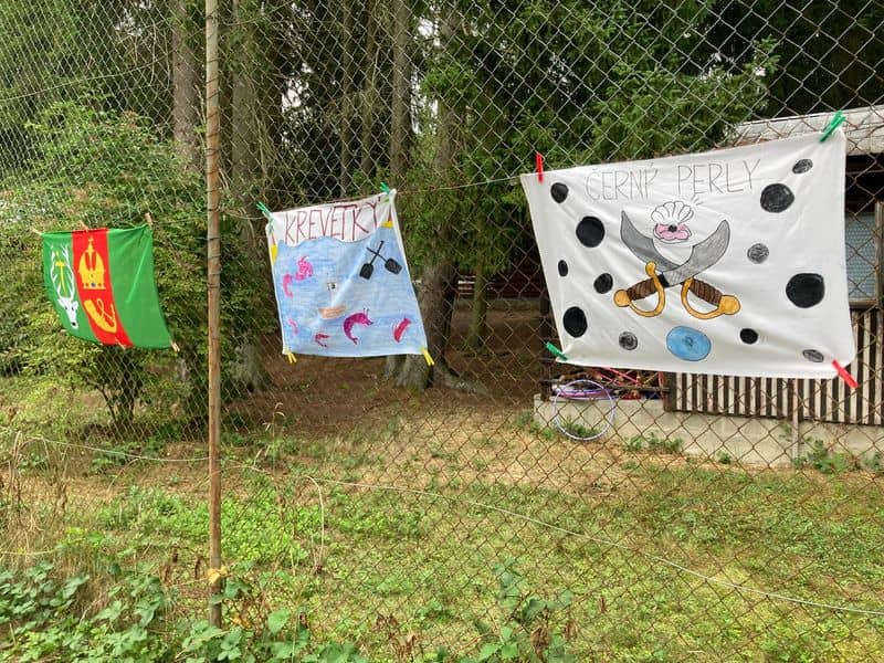 Tři dětské vlajky s obrázky a nápisy Krevety a Černé perly visí na plotě