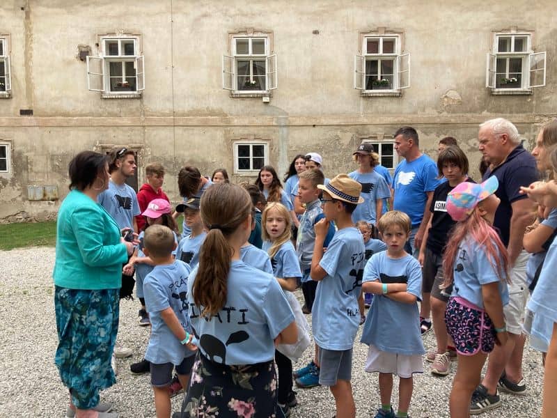 Skupina dětí a dospělých před starou budovou